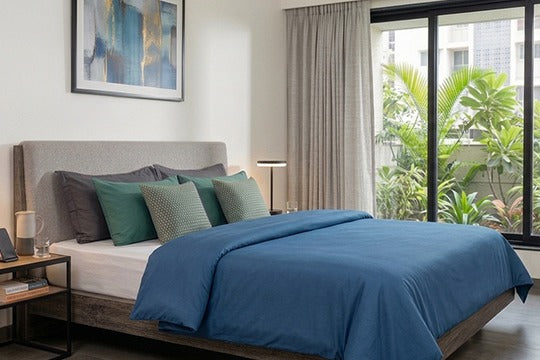 Modern Indian bedroom featuring a premium plain blue cotton duvet cover set without stitching patterns, styled with green pillows and a white fitted sheet on a wooden bed near a large window.