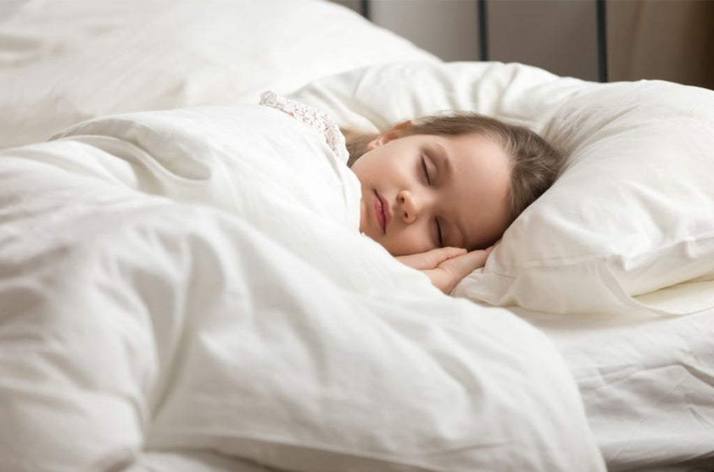 Child sleeping peacefully on soft white Pizuna cotton bedding.